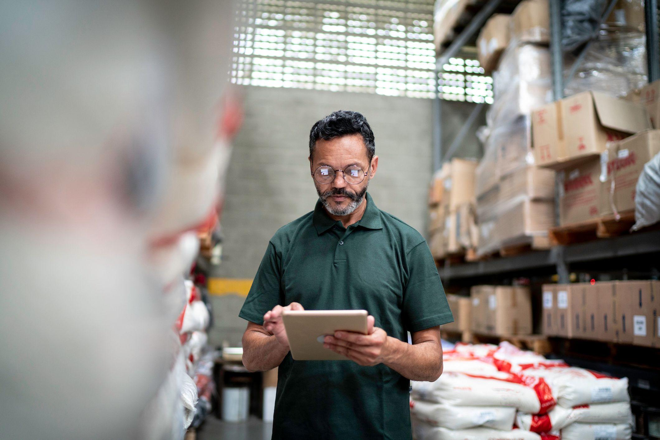 Trabalhador conferindo estoque em um armazém usando tablet.